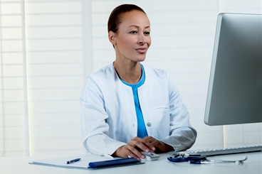 Nurse is sitting in front of a computer  and is doing an E-Learning course (landscape). Clipboard and stethoscope are lying on the table.